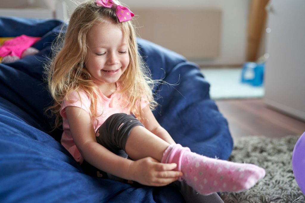 Happy little girl sitting in the beanbag and putting her pink socks on