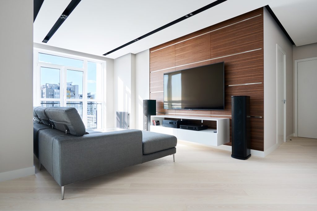 TV area in the modern Hi tech living room: French window, grey corner sofa, acoustic system and solid walnut wall panels